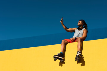 Black man taking selfie photo outside. Urban man posing with roller skates.