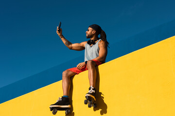 Black man taking selfie photo outside. Urban man posing with roller skates.