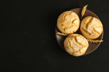 Freshly baked round buns on a plate on a black background. Selective focus with copy space, daylight