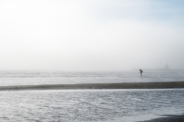 Fog on Baltic sea coastline at spring. Moody weather, mist. Person standing in distance