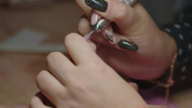 Female manicurist sanding fingernails with tool removing nail polish, close up