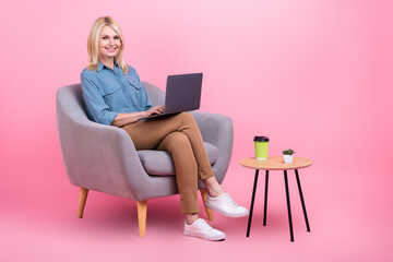 Fototapeta na wymiar Photo of attractive confident senior lady worker use netbook sit armchair office wear casual clothes isolated pink color background