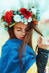 Sad, young woman wrapped herself in the flag of Ukraine with wreath of flowers on head. Patriotic...