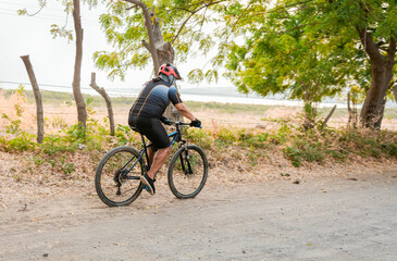 Fototapeta premium Fat cyclist on a dirt road surrounded by trees, Lifestyle of a chubby cyclist on the road, Professional cyclist on a dirt road