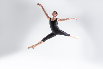 Fototapeta na wymiar Art Ballet of Young Caucasian Athletic Man in Black Suit Dancing in Studio Over White Background With Lifted Hands.