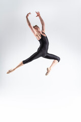 Fototapeta na wymiar Caucasian Ballet Dancer Young Athletic Man in Black Suit Posing Dancing in Studio On White.