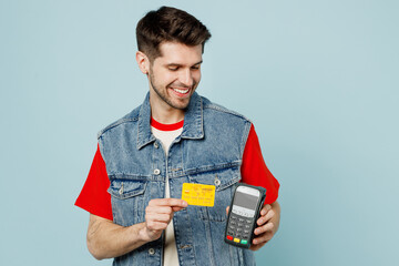 Young man wears denim vest red t-shirt casual clothes hold wireless modern bank payment terminal to...