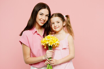 Happy fun woman wear casual clothes with child kid girl 6-7 years old. Mother daughter hold bouquet of daffodil flowers, hug, cuddle isolated on plain pastel pink background Family parent day concept