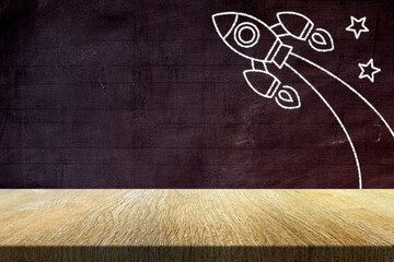 Wood Table with Retro Rocket in Chalk Drawing Style on Old Grunge Chalkboard Background, Suitable for Product Presentation Backdrop, Display, and Mock up in Back to School and Education Concept.