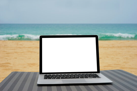 Laptop with blank screen for creative design on beach bed nearby beach and blue sea background. Computer notebook with clipping path for present landing page design mock up template © Chuenmanuse