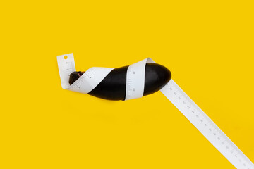 Eggplant with measuring tape on yellow background.