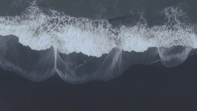 Aerial drone straight down waves crashing at Vik Iceland early winter fog at Black Sand Beach