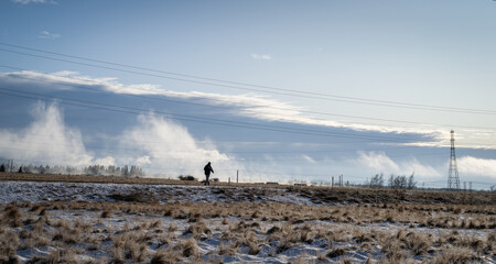 Man walking on snow-covered road with power pylon and power lines overhead. Twizel, South Island.