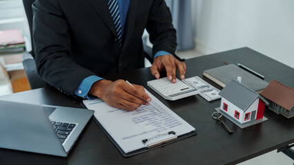 Mixed race asian indian man realtor chinese people with house model in formal suit in office at desk workplace.