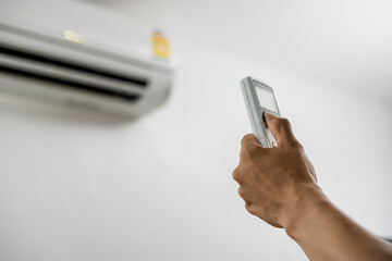 Fototapeta premium Air conditioner maintenance technician hand pressing remote control air conditioner background