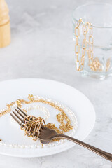 Jewelry bijouterie on a fork in a white plate at the dinner table. Shopaholism, waste of money, luxury concept.