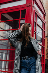 A girl in a gray coat stands by a red telephone booth