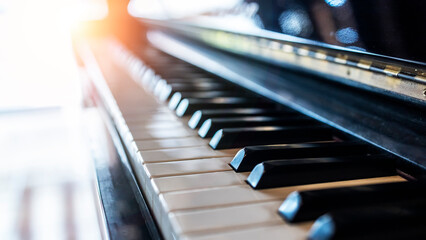 Piano keyboard in inclination angle with selective focus. Warm color toned image with orange light effect.Blur background with space.Black and white grand piano.Nobody or people. - obrazy, fototapety, plakaty