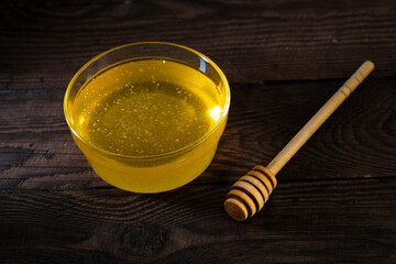 Glassware with honey and a wooden spoon for honey on a dark wooden table.