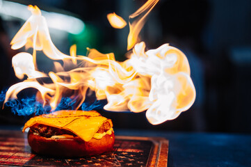 preparing a gourmet cheeseburger on restaurant kitchen with fire