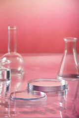 Various types of laboratory glassware and blank platform for display on pink water background. Cosmetics introduction stage on modern glass pedestal with laboratory equipment. Minimal concept.