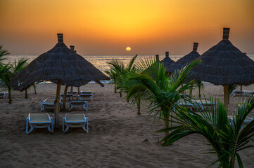 Sunset above Atlantic Ocean and a beach with palm trees, sunshades and sunbeds in Senegal, Africa
