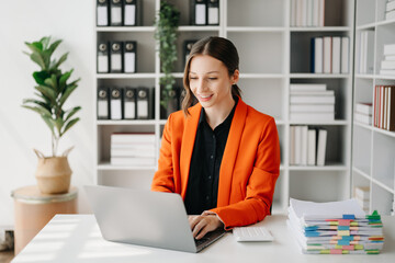 Confident business expert attractive smiling young woman typing laptop ang holding digital tablet on desk in office..