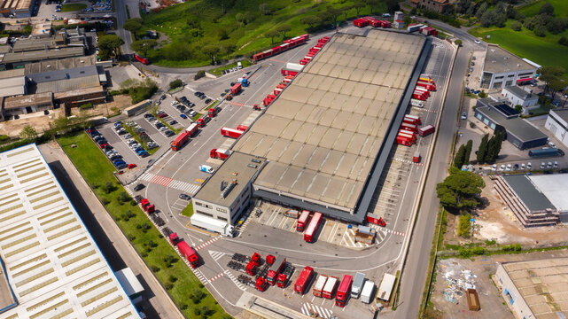 Pomezia, Italy - April, 2023: Aerial view of a large shed of the Bartolini shipping company. Warehouse for loading and unloading parcels. Many trucks are parked around the facility. Industrial area.
