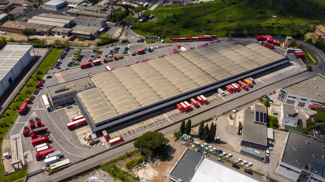 Pomezia, Italy - April, 2023: Aerial view of a large shed of the Bartolini shipping company. Warehouse for loading and unloading parcels. Many trucks are parked around the facility. Industrial area.