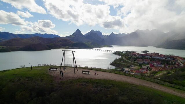 Aerial backward shot of parents swinging their child on the swing at the viewpoint in Ria&ntilde;o, a village in Le&oacute;n, Spain on the shore of a large reservoir in the Cantabrian mountains.