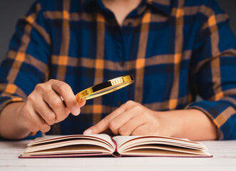 Close-up of hand holding a magnifying glass and reading a book while sitting at the table