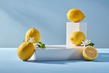 Pedestal for display cosmetic product of lemon extract with white empty podiums, lemons and white flowers on blue background. Lemon has many good uses for health and beauty. - obrazy, fototapety, plakaty