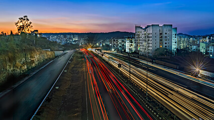 Fototapeta na wymiar Slow shutter speed image of light trails, beautiful sunset sky , buildings and flowing traffic on motorway.