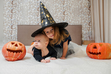 Little cute kids girls in Halloween costumes with carved pumpkins at home. Caucasian baby siblings...