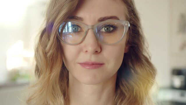 Attractive young serious female face in spectacles. The woman has short, curly blond hair. Light shade of lipstick on lips, minimum of make-up. High quality 4k footage