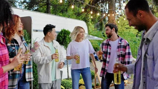 Mixed-race party of friends with beer in their hands. Have fun listening to music and dancing at festive summer parties near the travel trailer. Happy multi ethnic young people.