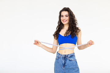 Young woman measuring her waist and showing how much weight she lost in jeans, on a white...