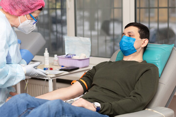 man donor in medical mask for bone marrow donation blood in laboratory. male hand holding red ball, prevention of diseases, illness hemodialysis transfusion in hospital. soft focus