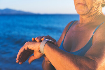 Senior woman in a swimsuit at the beach, using smartwatch