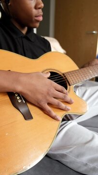Teenager playing acoustic guitar on sofa at home