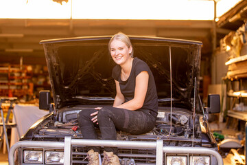 confident female mechanic sitting on a 4wd she has been working on in garage repair shop