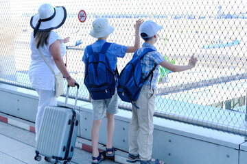 woman with suitcase, two children, young traveler, boys of 8-10 years old with backpacks in outdoor terrace of airport, concept of vacation, long journey, air travel insurance, aircraft observations