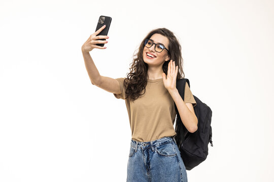 Happy young woman student making selfie photo on smartphone and winking isolated on a white background