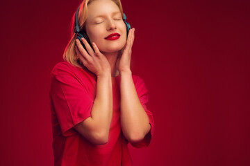 A happy girl listening music isolated on red background with wifi headphones and smiling with eyes closed.