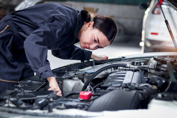 Fototapeta na wymiar Beautiful female auto mechanic in uniform working with engine vehicle at garage, car service technician woman checking and repairing customer car at automobile service center, vehicle repair service.