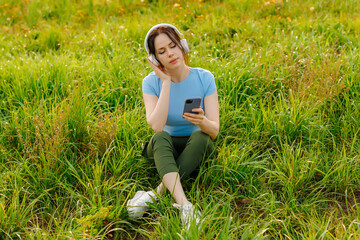 Beautiful happy young woman with headphones listening music lying on grass