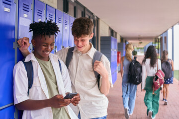 Two Male Secondary Or High School Students Outdoors At School Looking At Mobile Phone