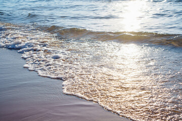 Sea waves with foam, illuminated by rays of setting sun, roll on coastal sand. Meditation and relaxation. Tourism .