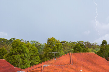 Lightning bolt strike against storm clouds about suburban house roof with red tiles