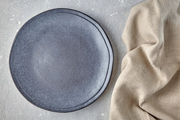 An empty gray ceramic plate and a rough linen napkin on a gray concrete table. Background for...